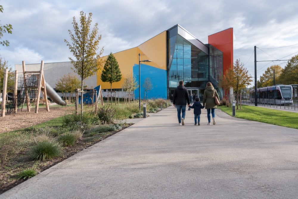 A family walking a wide paved path toward a modern museum entrance in late afternoon light