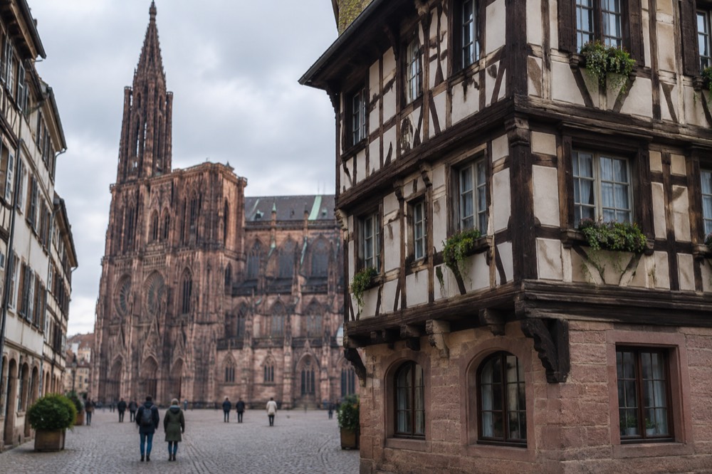 Half-timbered facade of a tall corner house on a cobbled square beside a cathedral