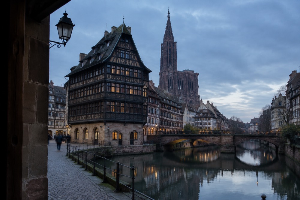 Timber-framed houses reflected in a calm river channel with stone bridges
