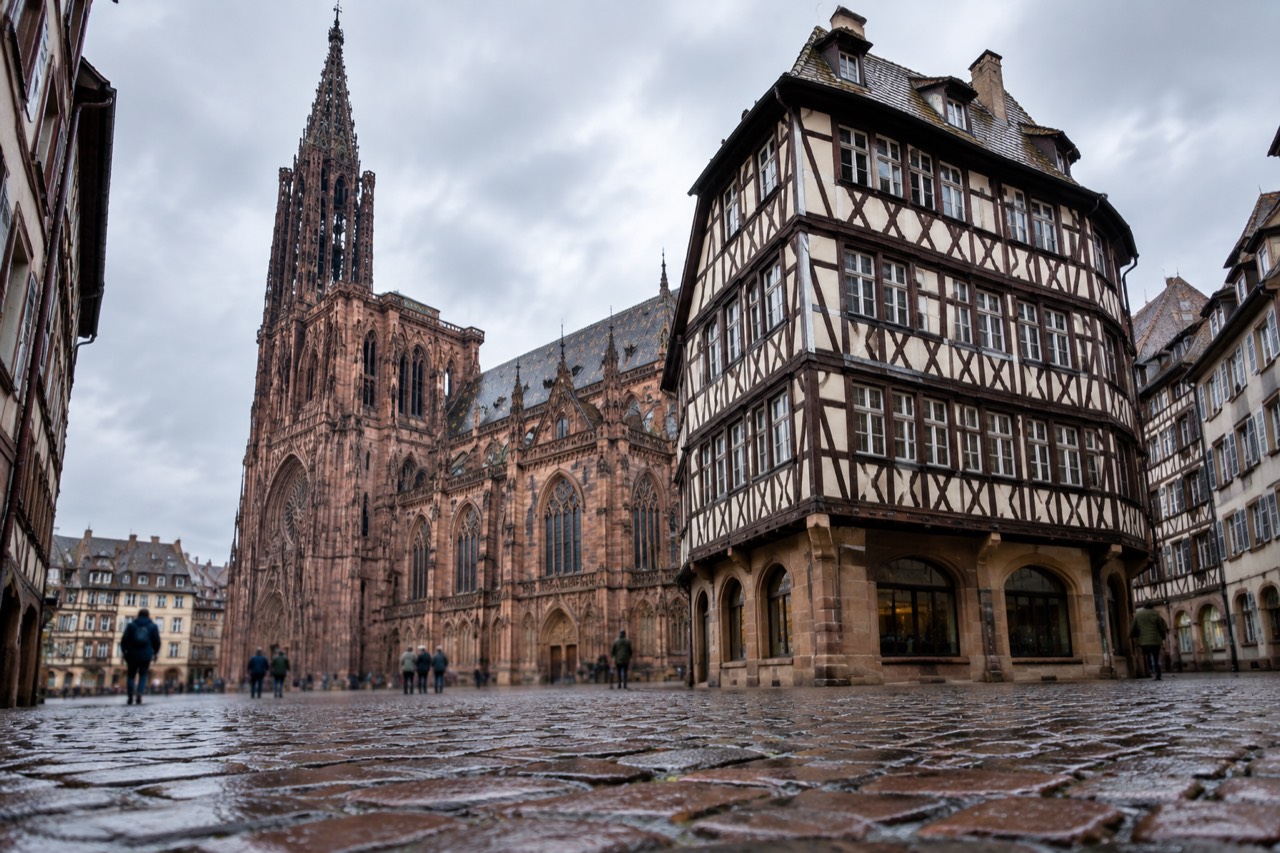 Half-timbered facade of a tall corner house on a cobbled square beside a cathedral