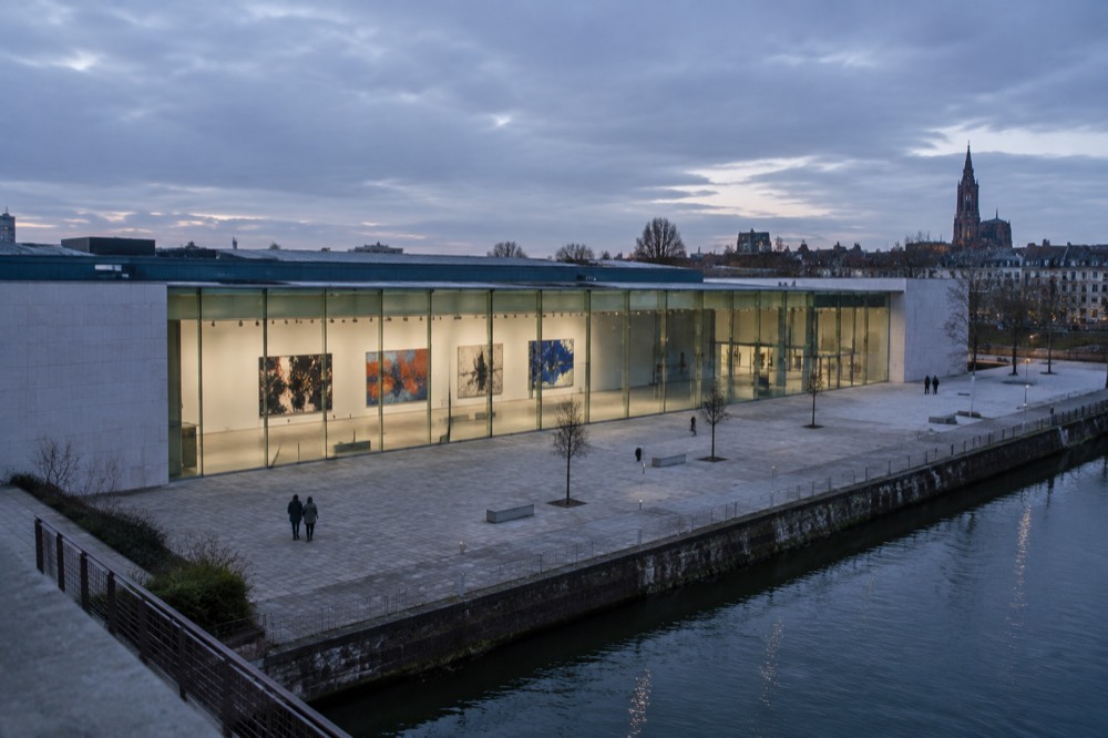 A bright gallery hall with white walls and large abstract paintings hung in a row