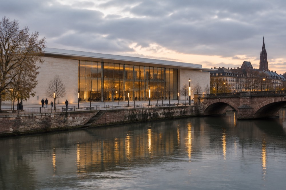 A dusk view of a lit museum facade reflected in the river with an old stone bridge alongside