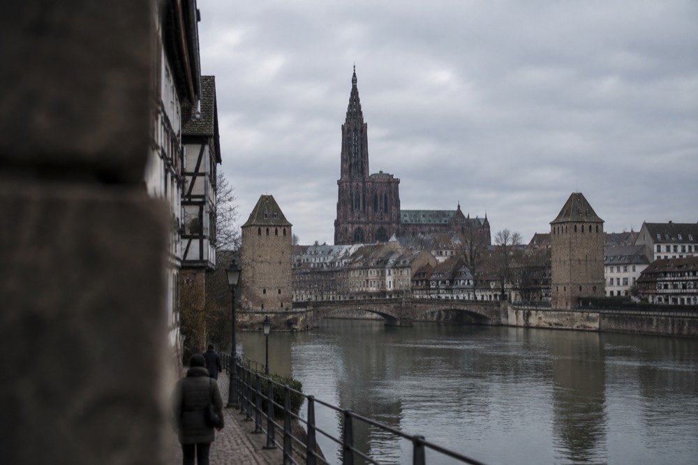 Wide view of the Ill in Strasbourg with the quay, old rooftops and bridge towers along the river