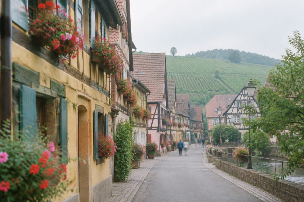 Narrow main street of a wine village lined with flower-decorated half-timbered buildings