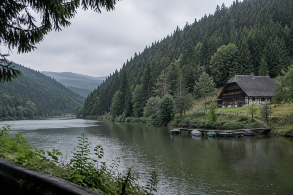 Calm lake at the foot of forested hills with small boats at a wooden pier