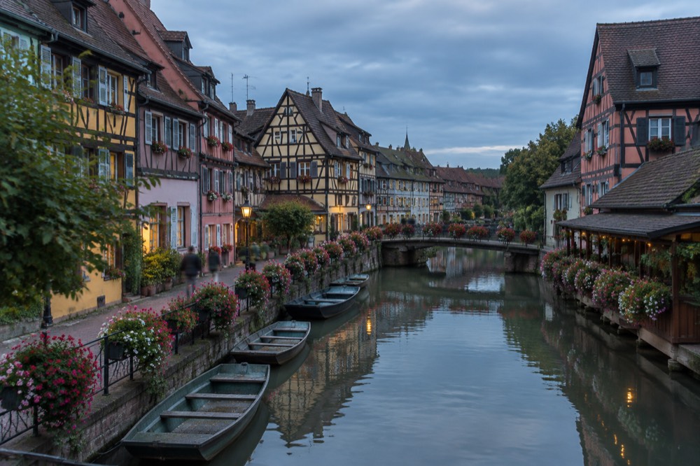 Flower-lined canal in Colmar's Little Venice quarter with small boats moored at the bank