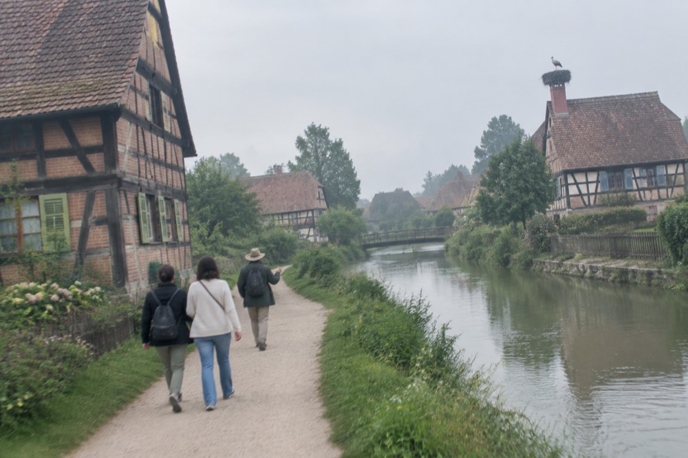 A guide leading a pair of visitors along a riverside lane lined with timbered houses