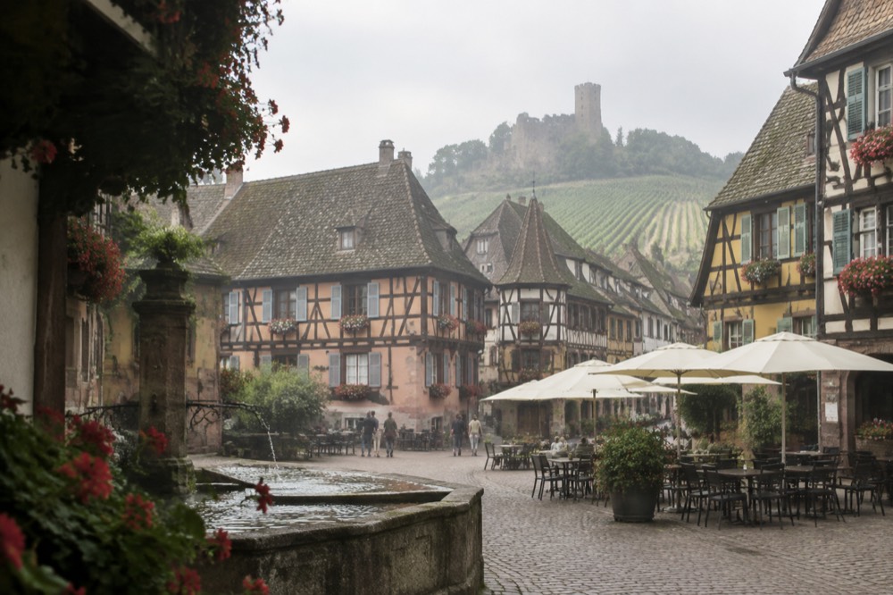 Village square with outdoor tables and half-timbered buildings in Eguisheim