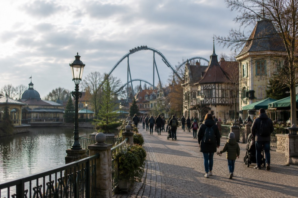 Families walking along a wide themed boulevard with ride structures behind the rooftops