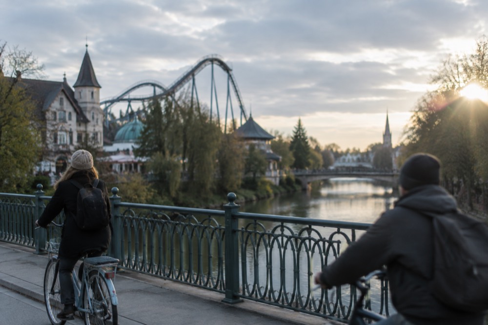 Cyclists crossing a bridge over a city river with a spire in the distance