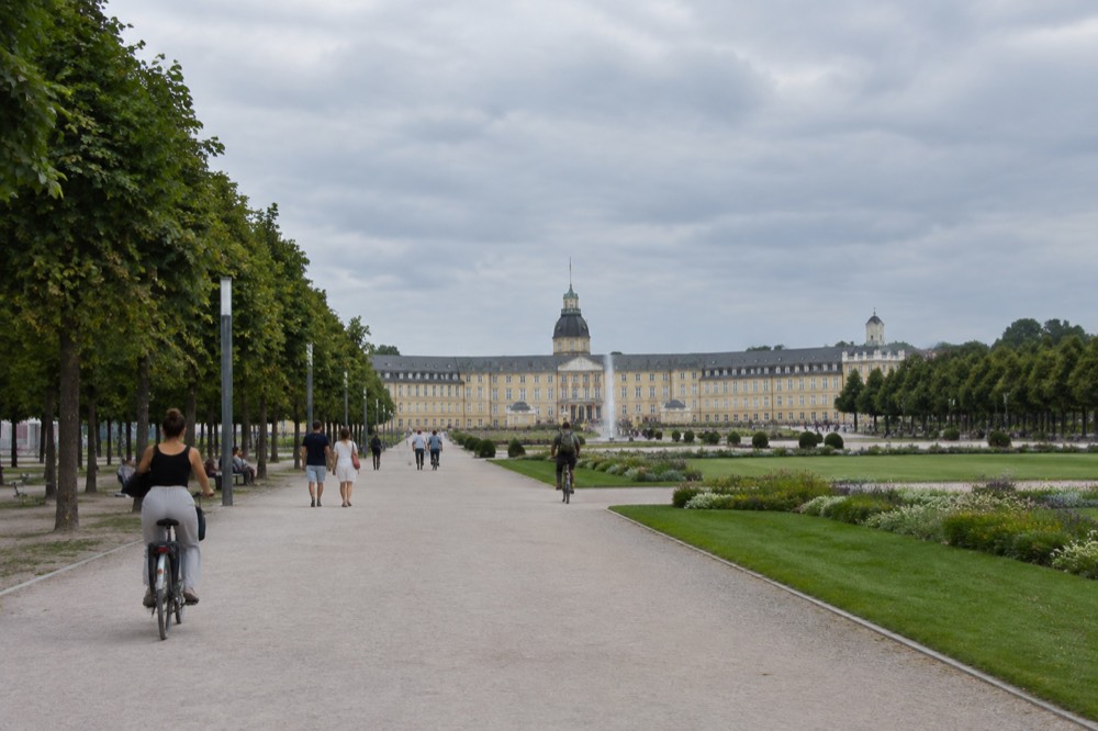 Tree-lined avenues radiating from a palace square with cyclists and pedestrians in summer light