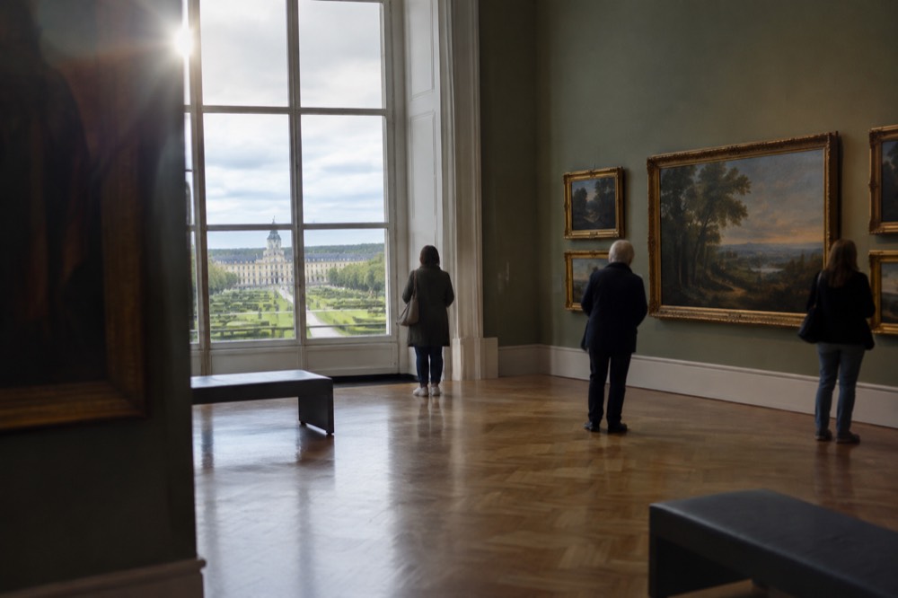 A museum interior with paintings on tall walls and visitors viewing the collection quietly