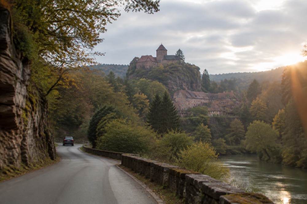 Country road winding through wooded Vosges hills with sandstone cliffs on one side