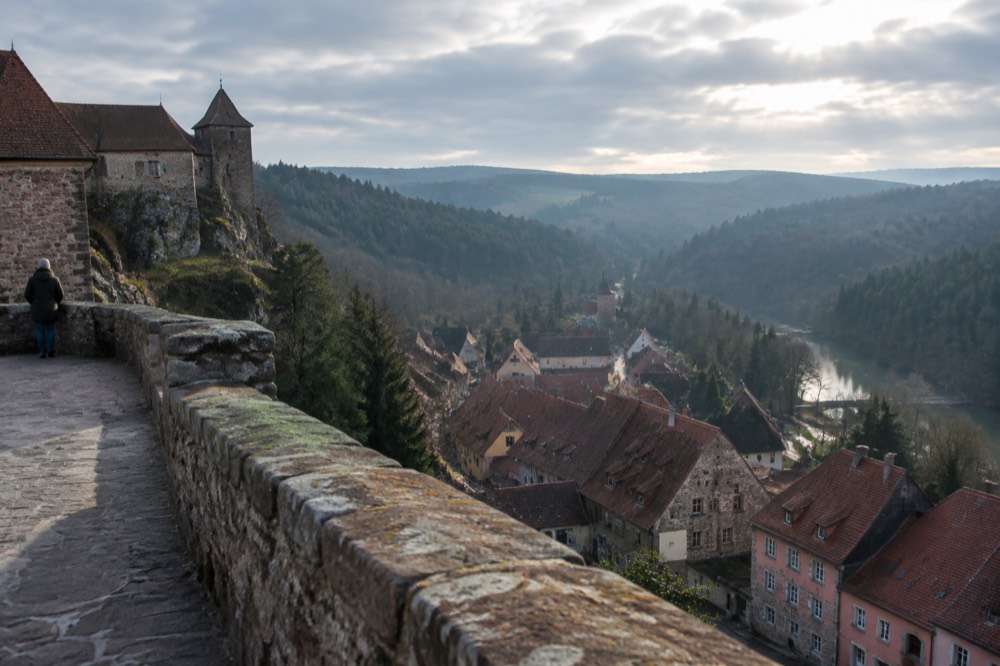 View over red rooftops of the village from the castle terrace with layered forested hills fading into haze