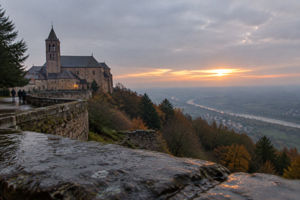 The summit terrace at sunset with the abbey silhouette and the plain of Alsace fading into haze below