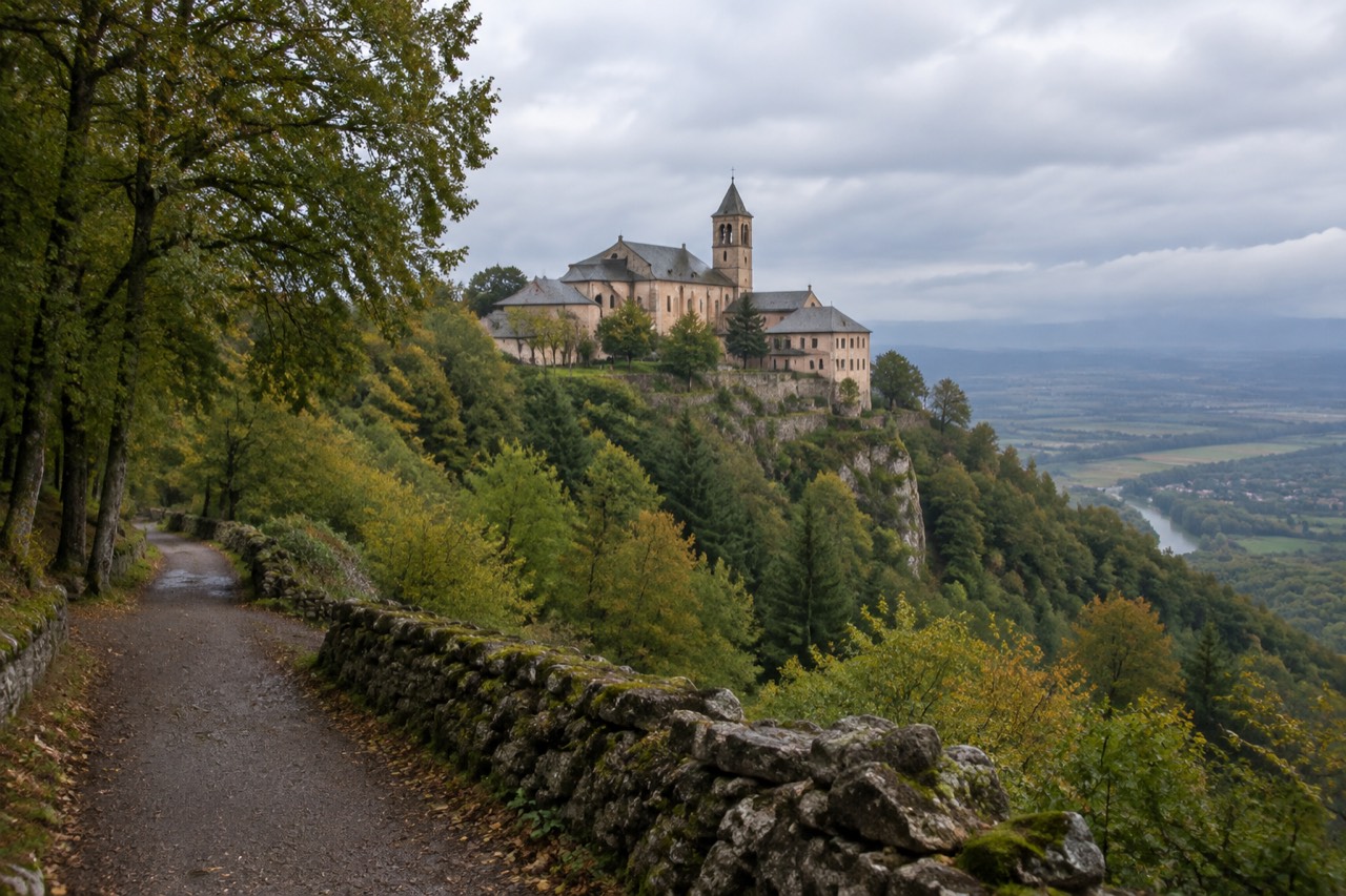A mountaintop abbey with pale walls and a bell tower seen from a forest road on a ridge in the Vosges foothills