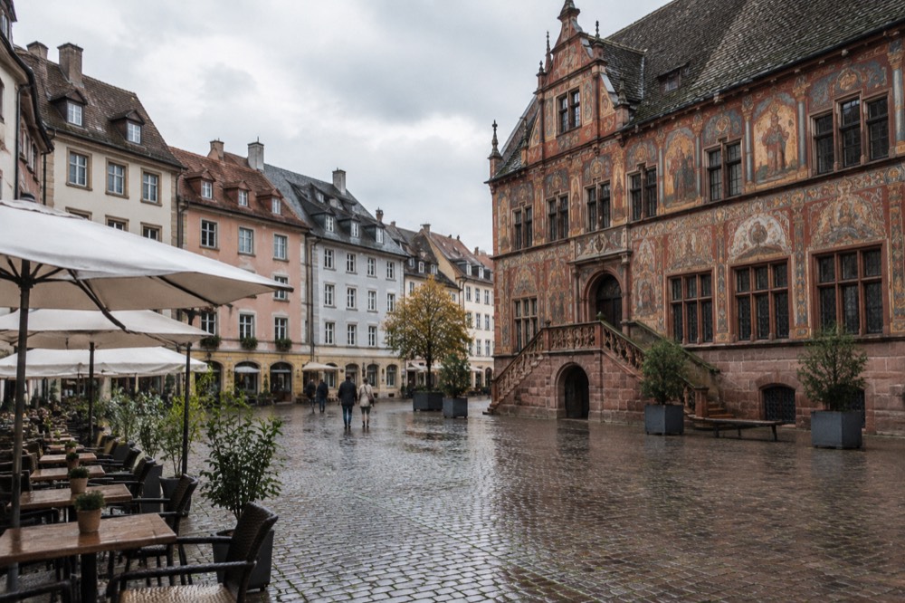 A pedestrian square with historic facades and outdoor cafe tables in Mulhouse old town