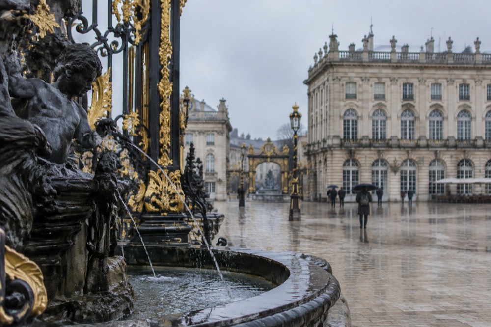 Gilded black ironwork gate and fountain on a grand square with stone facades