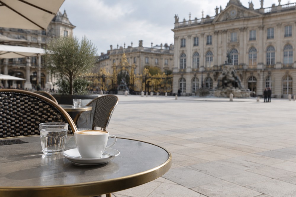 Cafe terrace tables set out along a stone square with ornate facades