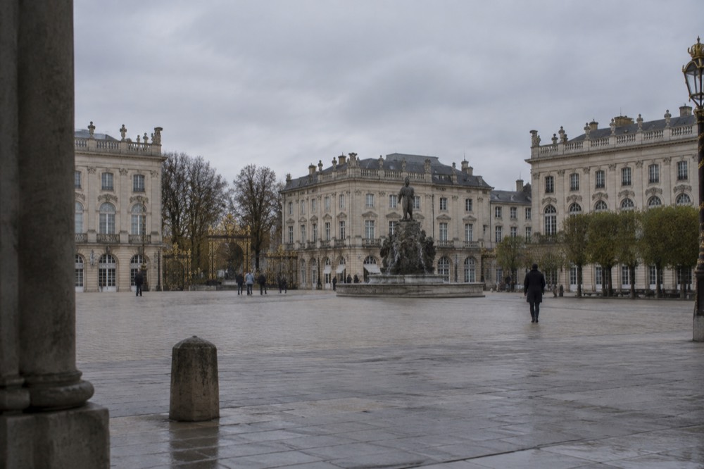Tree-lined square with symmetrical classical facades and a stone fountain