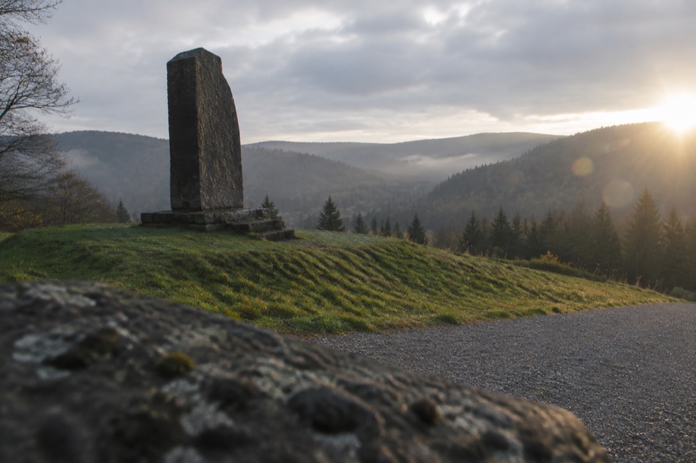 A stone memorial monument standing on a grassy ridge above a wide forested valley