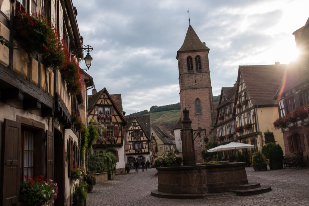 Half-timbered houses with steep roofs and flower boxes lining a narrow street in an Alsatian wine town