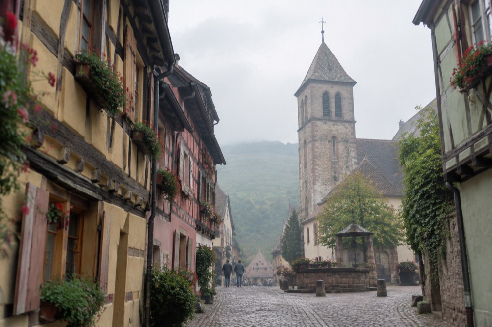 A narrow cobbled lane between coloured half-timbered houses with window boxes in a wine village