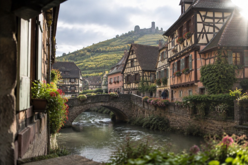 A stone bridge over a small river beside half-timbered houses in an Alsatian village
