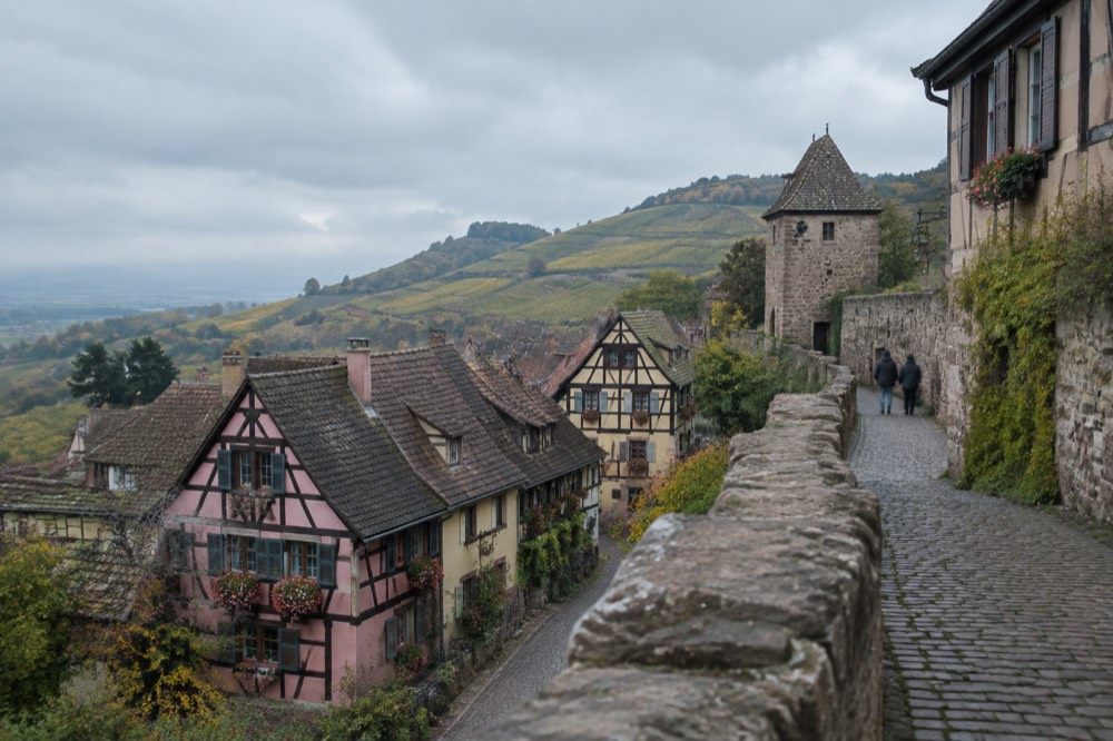 A stone rampart path leading past old village walls toward open countryside