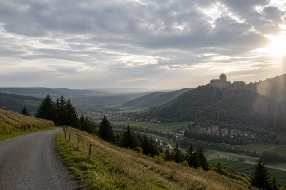 A stone castle on a wooded hill overlooking a wide valley of vineyards