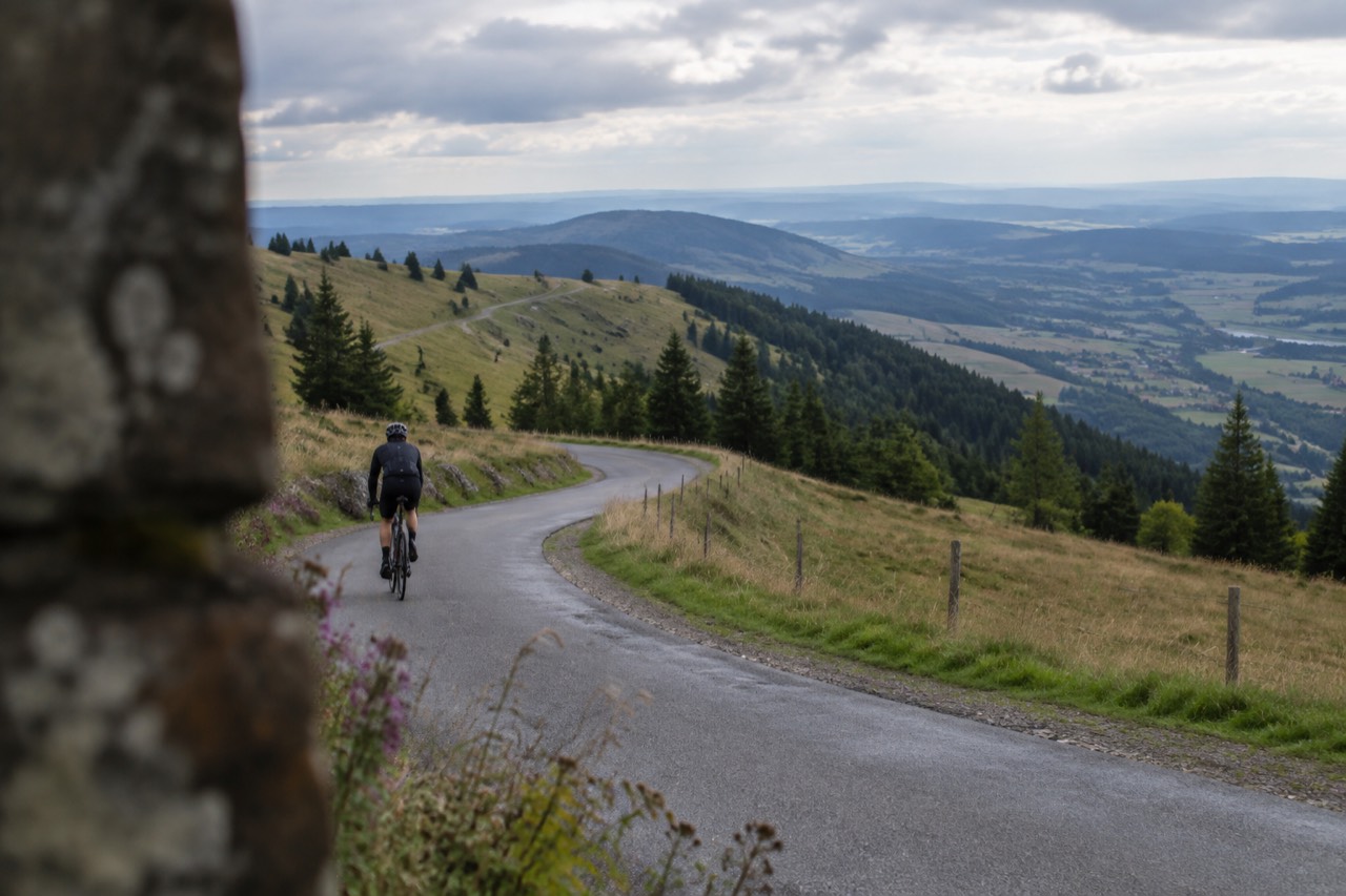A narrow ridge road curving between grassy Vosges meadows with views over a wide plain