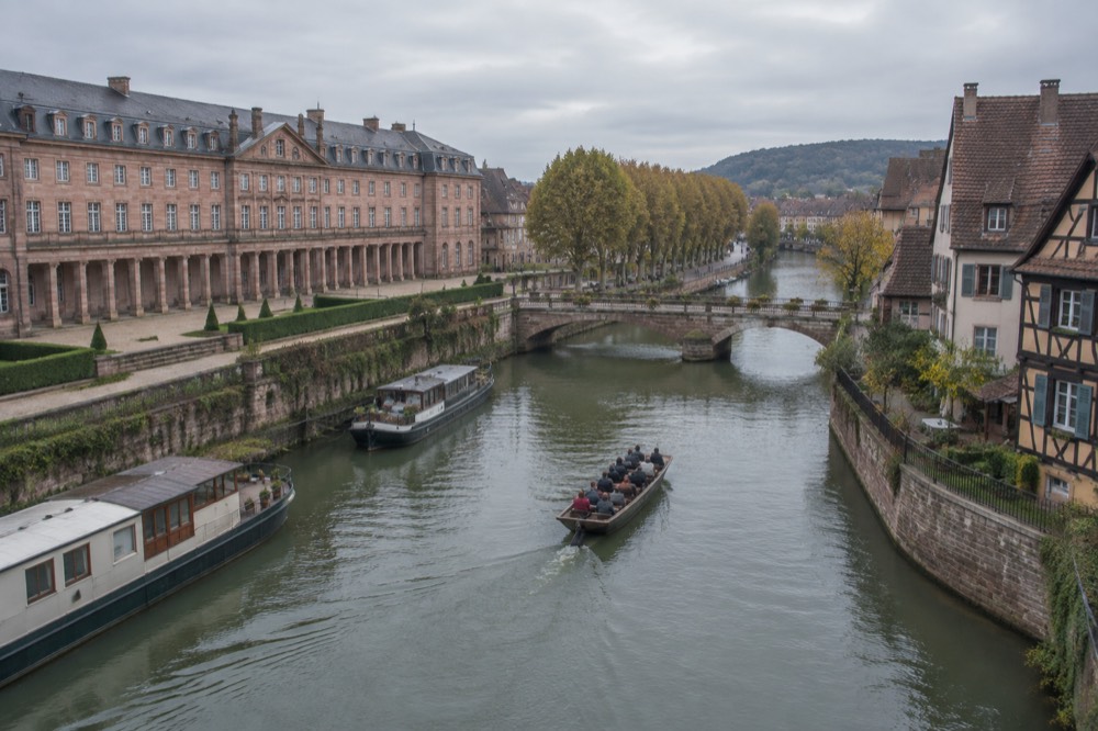 A flat-bottomed boat gliding on a narrow river past half-timbered houses