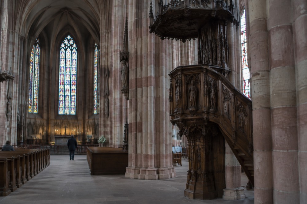 The Gothic interior of St. George's Church in Sélestat, with tall pillars, stained-glass windows and a carved wooden pulpit