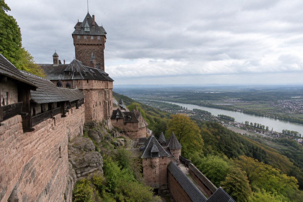 A restored medieval castle standing on a forested sandstone ridge in Alsace