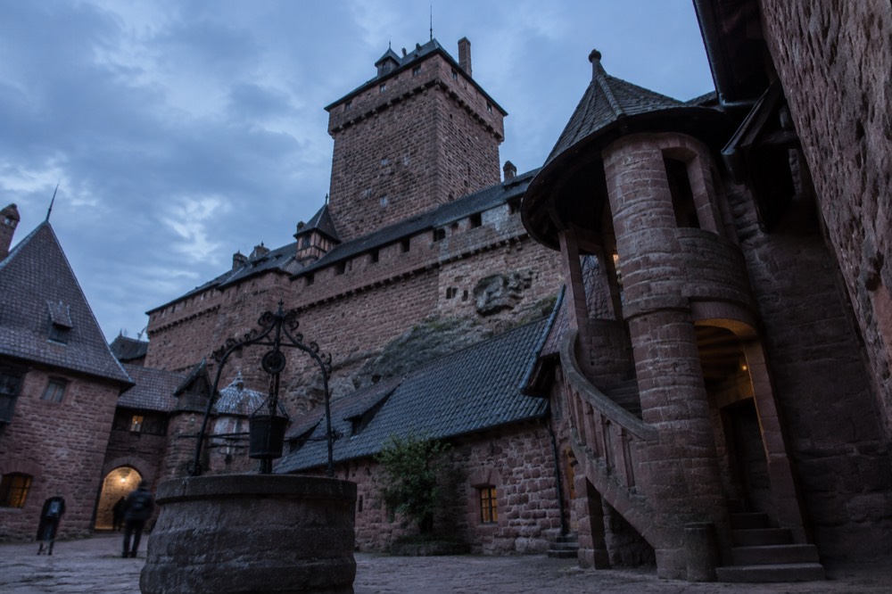 A castle courtyard with a stone well and a spiral staircase inside a fortress
