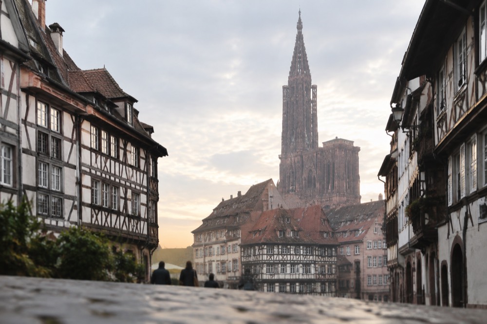 Strasbourg Cathedral's single spire rising above red rooftops at dusk