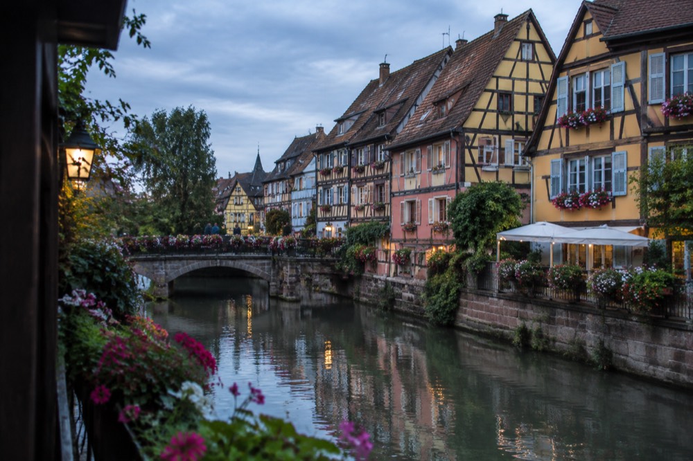Flower-decorated canal in Colmar, France, with colourful half-timbered facades