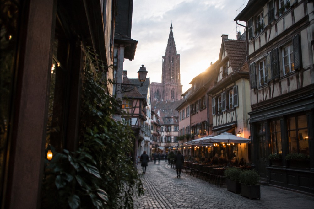 A narrow evening street with small lit restaurant fronts away from the main squares