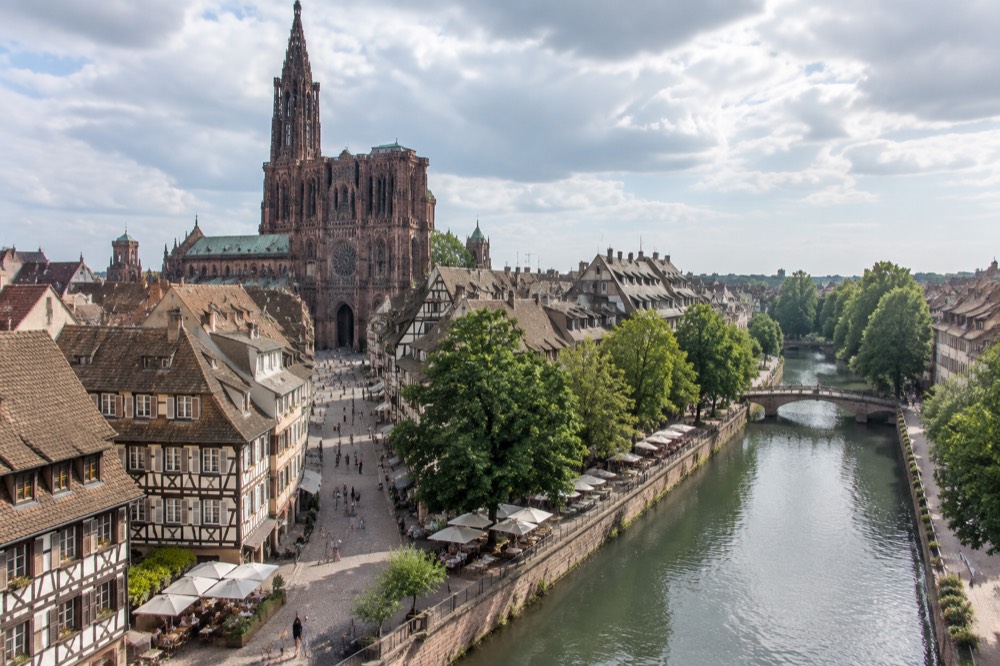 A tree-lined canal in Strasbourg on a bright summer day with café tables along the bank