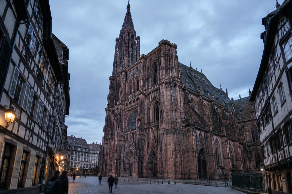The pink sandstone facade of Strasbourg Cathedral seen from a cobbled square