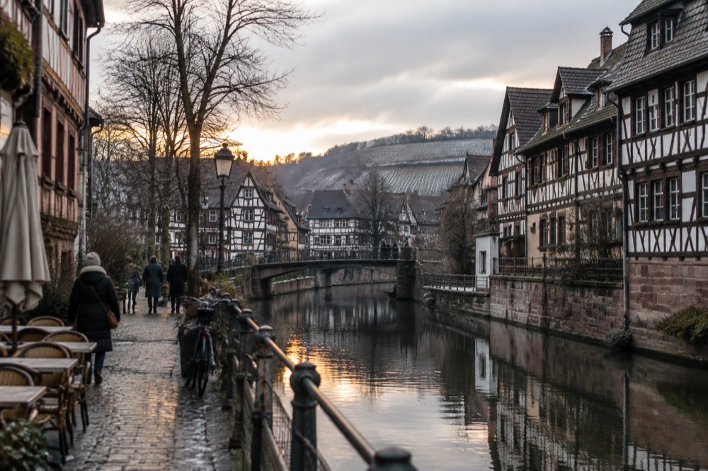 An Alsatian wine route village street with half-timbered houses and vineyard hills behind in winter light