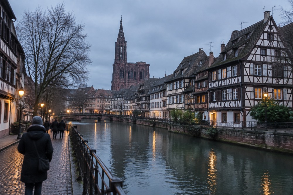 Half-timbered houses along a canal in Strasbourg at dusk with early lights