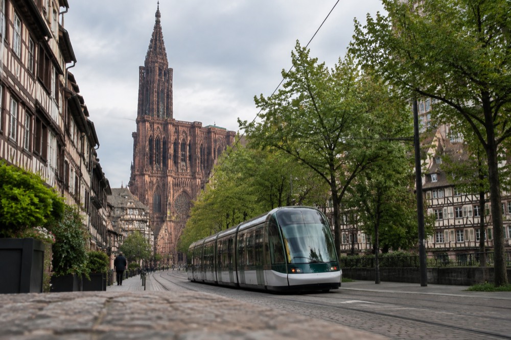 A modern Strasbourg tram travelling along a tree-lined street in the city centre