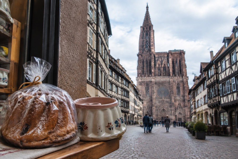 A wrapped kougelhopf cake beside a ceramic fluted baking tin in a Strasbourg kitchen shop