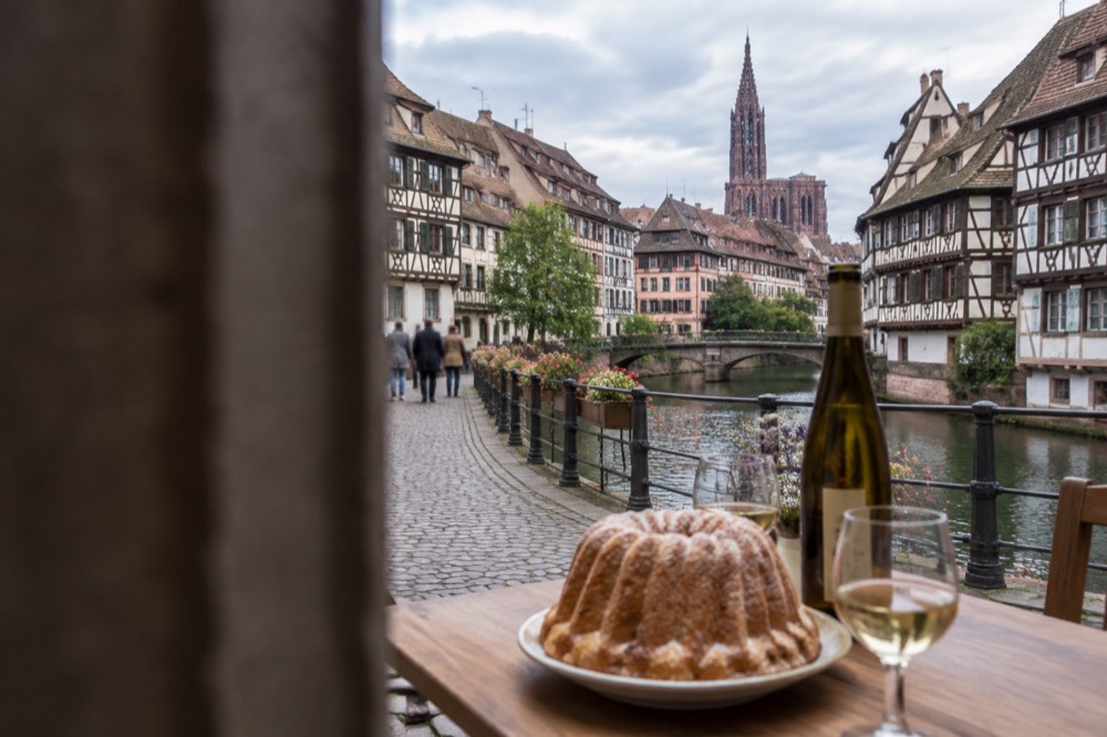 A kougelhopf ring cake on a table with an Alsatian wine bottle and glasses in a village bakery