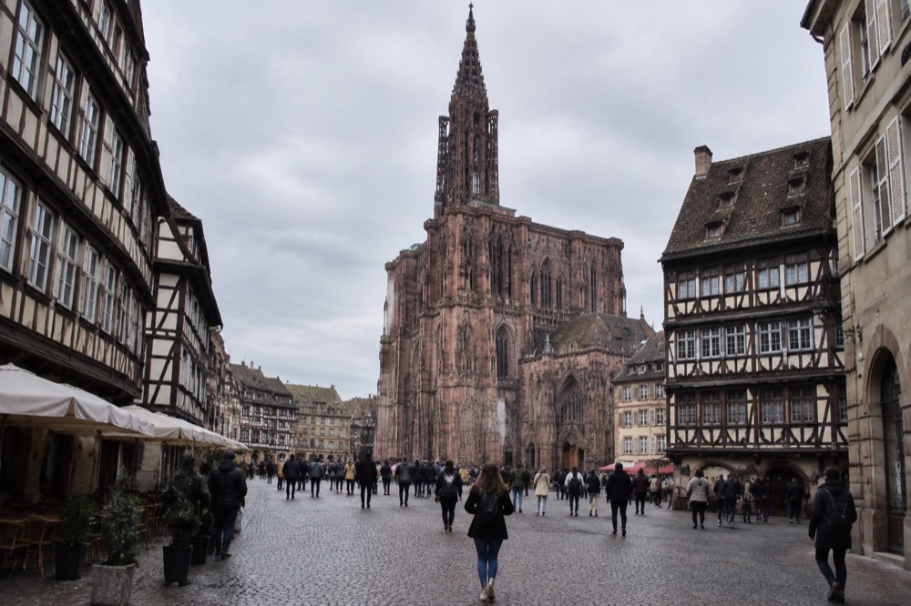 A Gothic cathedral facade of pink sandstone rising above a crowded European square