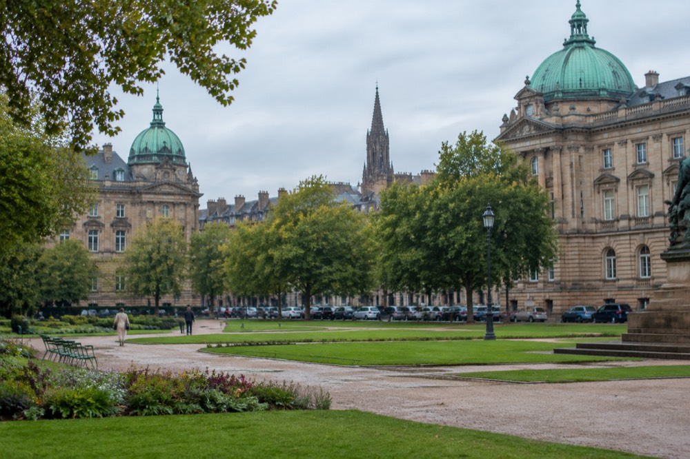 A row of parked cars along a tree-lined street with a church spire behind