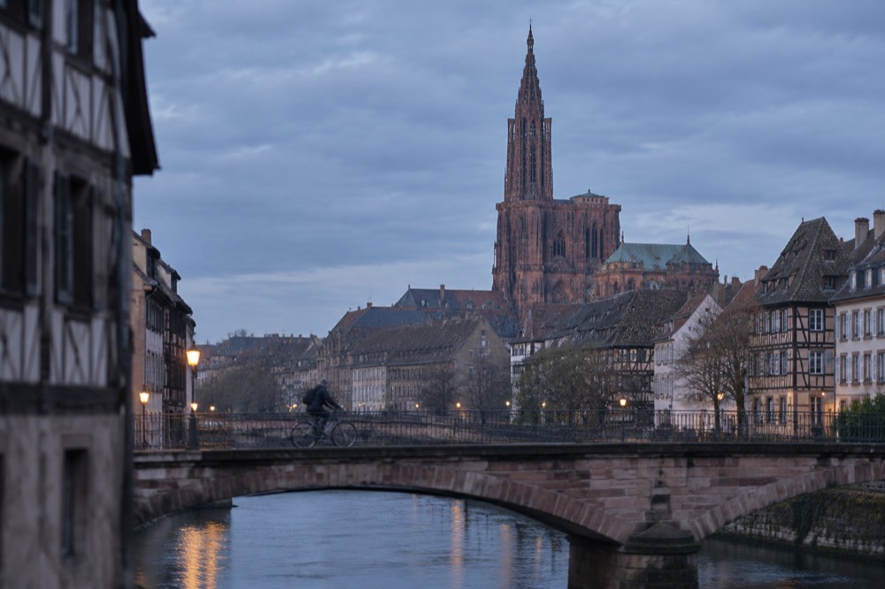 A cyclist crossing a bridge over the Ill with the cathedral spire in the distance
