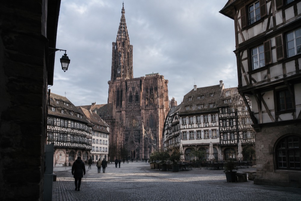 A wide square in Strasbourg with the single-spired cathedral rising above rooftops