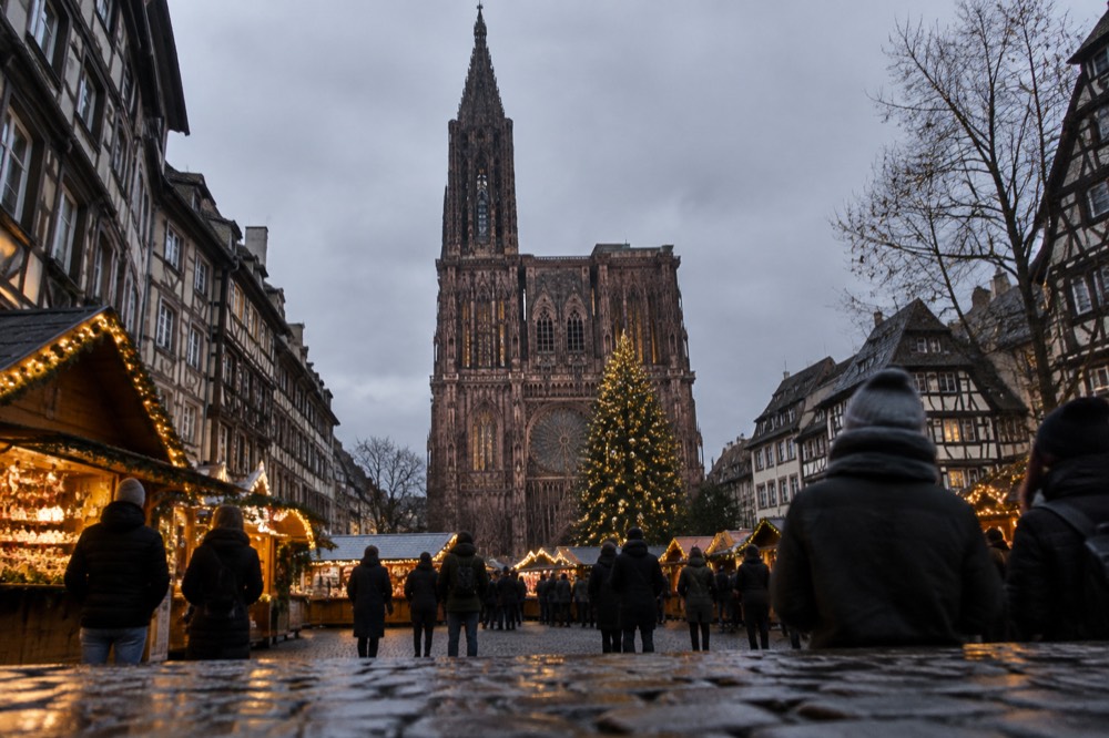 A Christmas market square in Strasbourg at dusk with illuminated chalets and a large tree